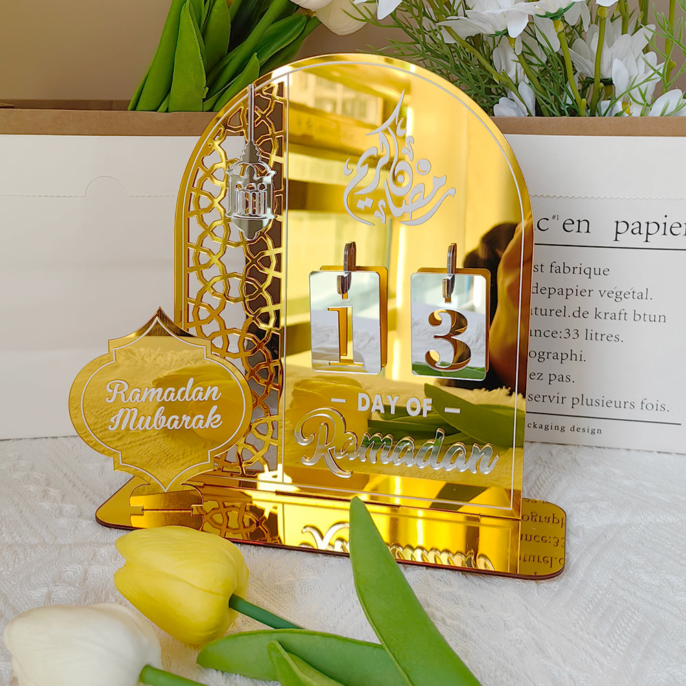 Gold Ramadan decorative item with 'Ramadan Mubarak' and 'Day of Ramadan' text, surrounded by flowers on a white surface.