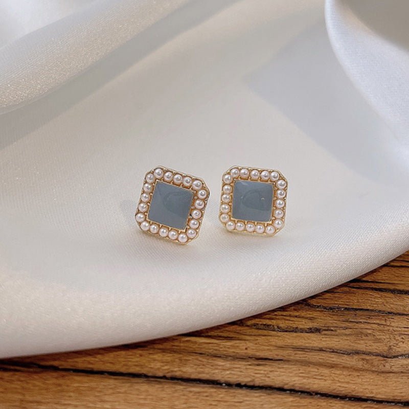Flat lay of geometric square frame pearl earrings on neutral background