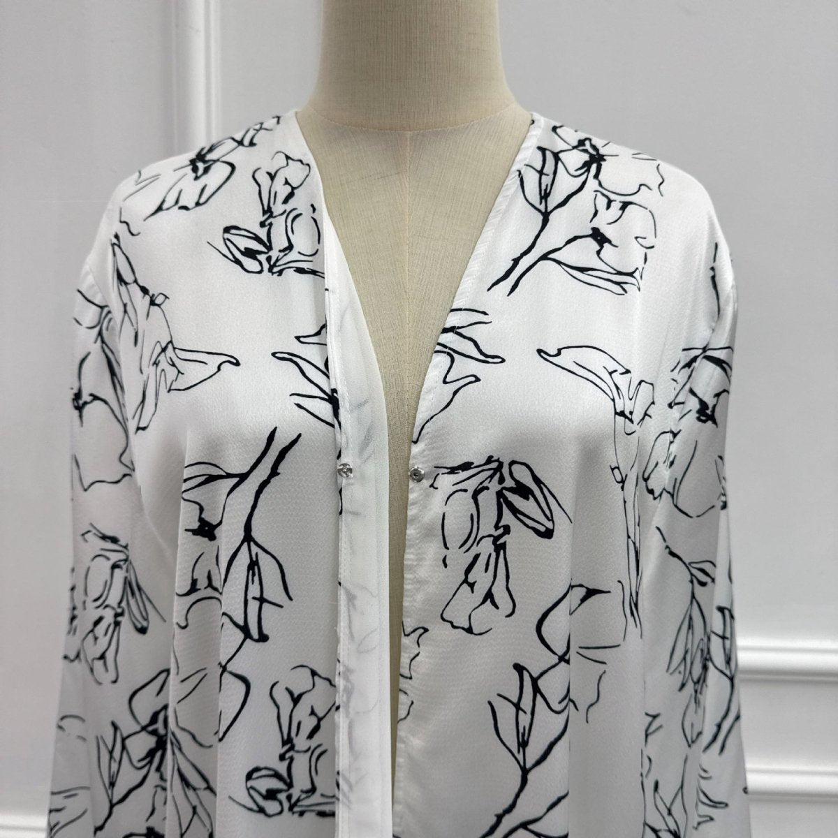 Matching hijab laid flat alongside ink-brush floral double-layer open abaya